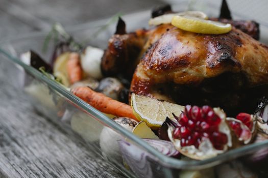 Plat de poulet rôti agrémenté de légumes colorés et de quartiers de citron, servi dans un plat en verre.